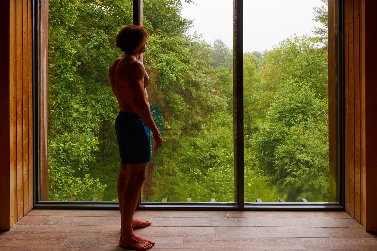 Man stood admiring the views of the forest from inside the Treetop Sauna.